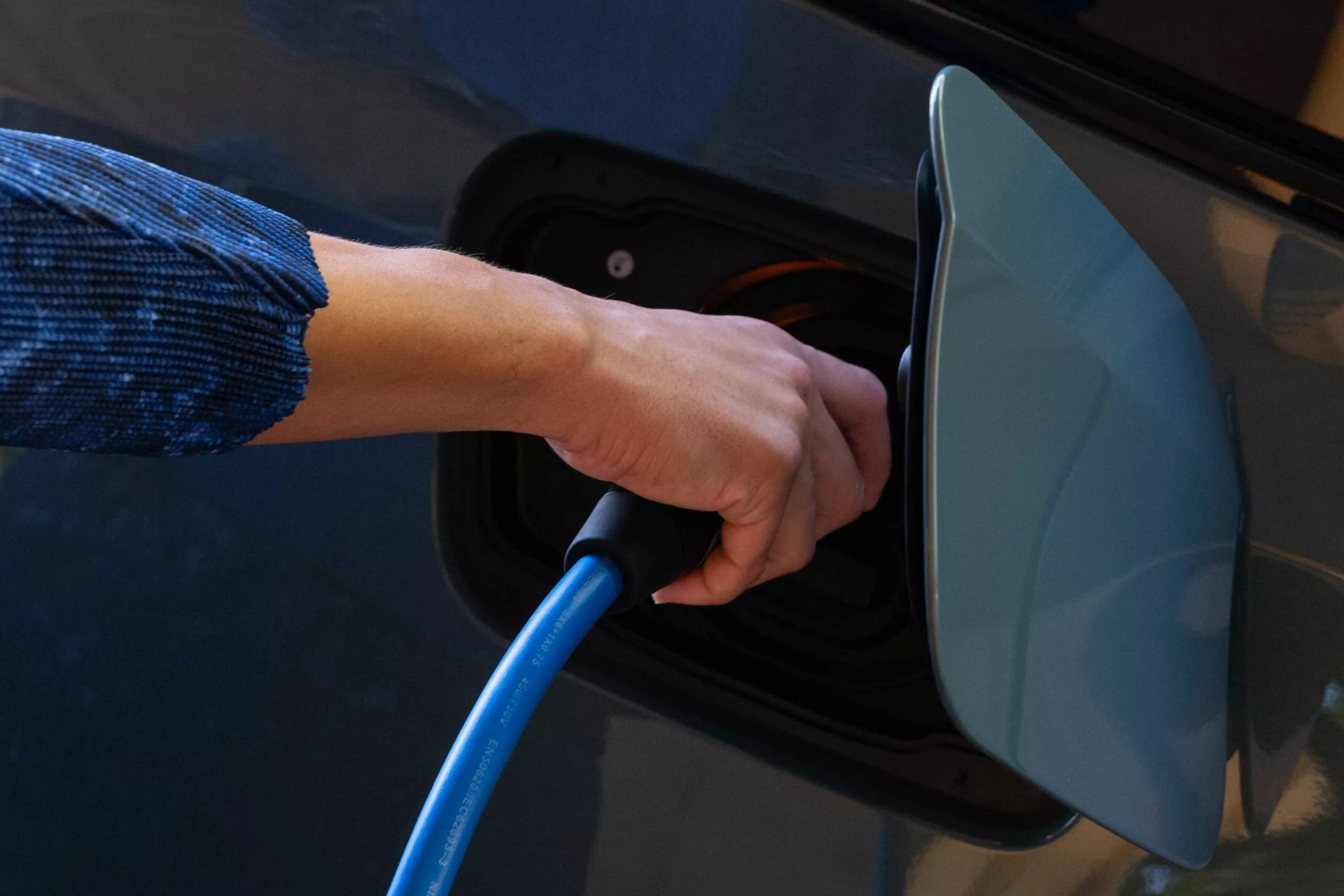 Nahaufnahme einer Hand, die ein blaues Ladekabel in den Ladeanschluss eines Elektroautos steckt