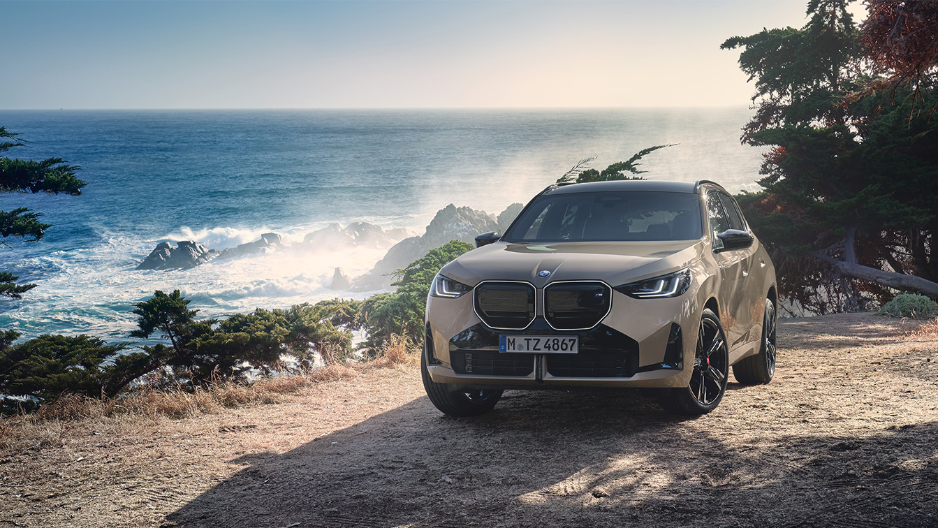 Gemini hat gesagt Das Bild zeigt den neuen BMW X3 in einem sandfarbenen Goldton, der auf einer Anhöhe direkt an einer rauen Küste parkt. Im Hintergrund bricht sich das Meer an schroffen Felsen, während das warme Sonnenlicht eine abenteuerliche und zugleich luxuriöse Atmosphäre schafft. Mit seiner markanten, großen Doppelniere und den dunklen Akzenten wirkt das SUV in dieser naturbelassenen Umgebung besonders robust und präsent.