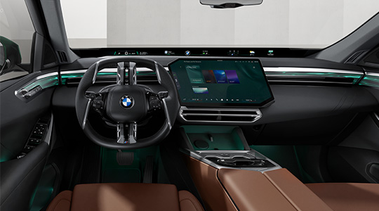 Moderner Innenraum des neuen BMW X5 mit BMW Lenkrad, großem zentralem Touchdisplay, digitaler Instrumentenanzeige und türkisfarbener Ambientebeleuchtung. Die braunen Sitze und die elegante Mittelkonsole unterstreichen das hochwertige Design