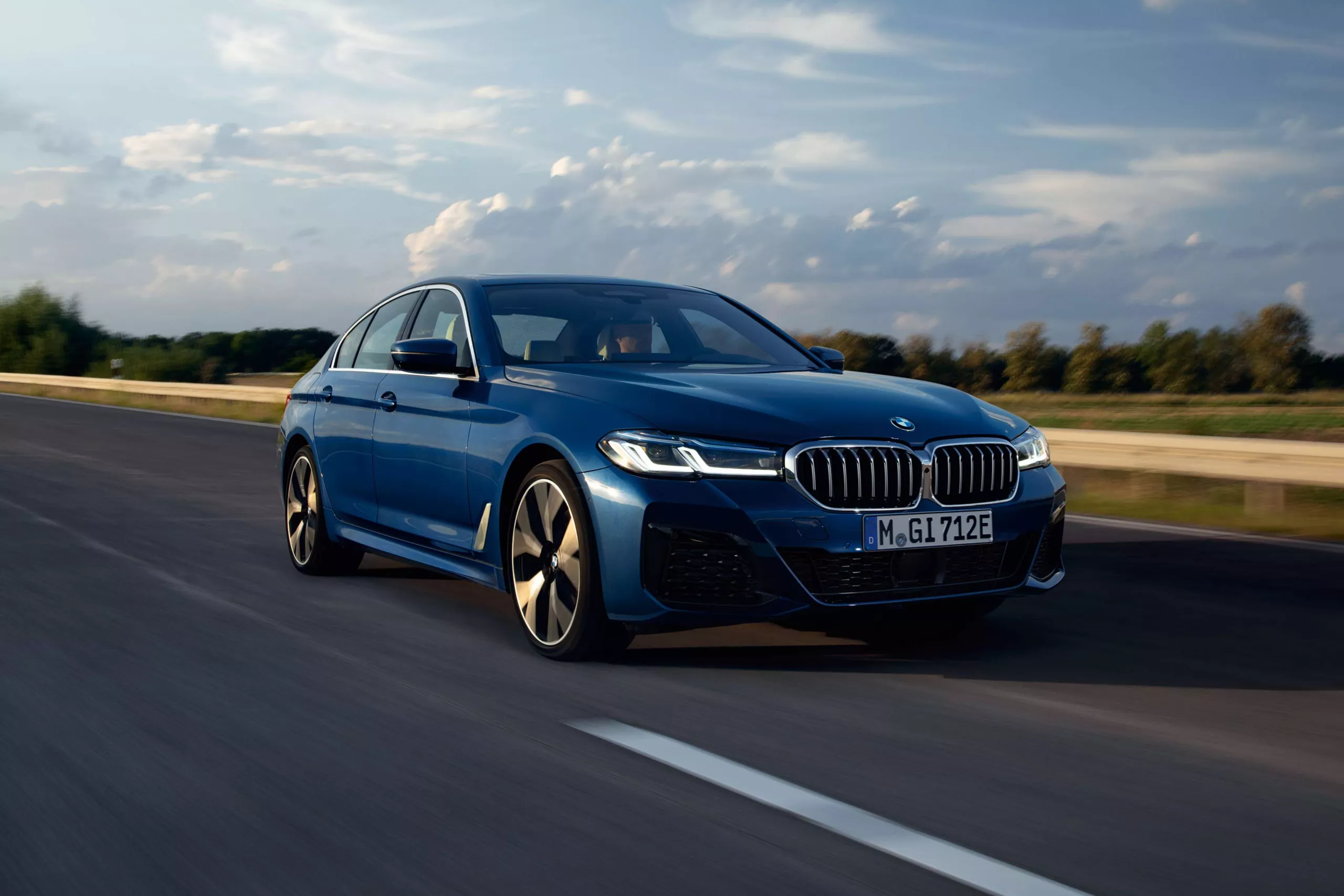 BMW Müller Leistungen Dunkelblauer BMW fährt dynamisch auf einer Straße mit bewölktem Himmel.