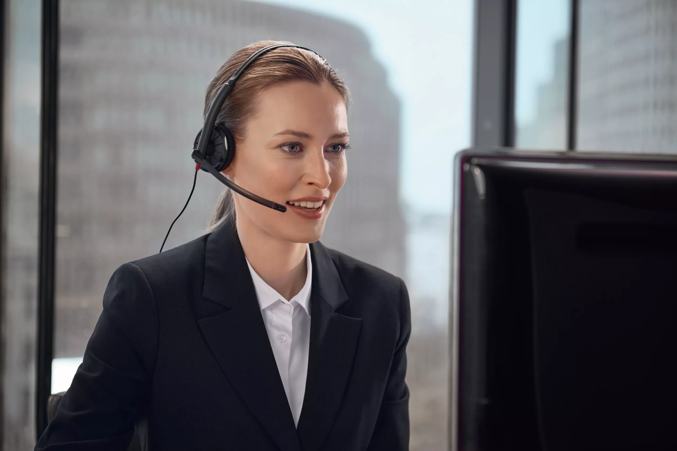 BMW Müller PREMIUM SELECTION Frau mit Headset und Mikrofon lächelt während eines Gesprächs am Computer in einem Büro.