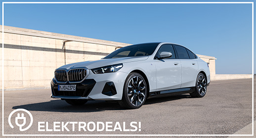Dreiviertel-Vorderansicht einer hellgrauen BMW i5 Elektro-Limousine mit Kennzeichen 'MDY 237E', parkend auf Asphalt vor einer Betonmauer. Mit 'Elektrodeals!'-Logo."