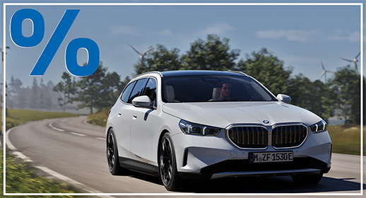 Weiße BMW 520i Touring (Kombi) auf einer Landstraße mit Windrädern im Hintergrund; blaues Prozent-Symbol oben links.