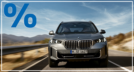 Frontansicht eines grauen BMW X5 SUV auf der Autobahn vor Gebirgspanorama; blaues Prozent-Symbol oben links.