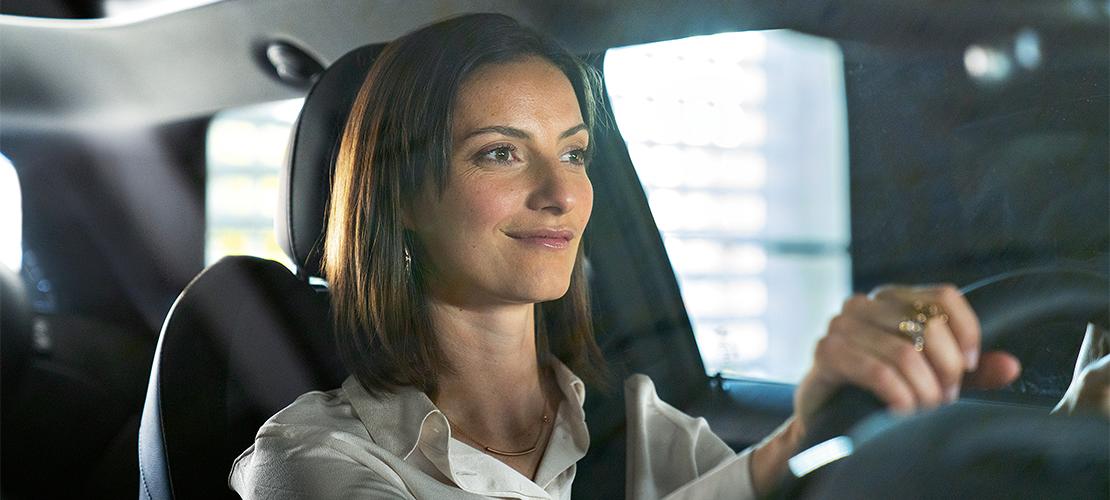  Eine lächelnde Frau fährt ein Auto und blickt zur Seite.