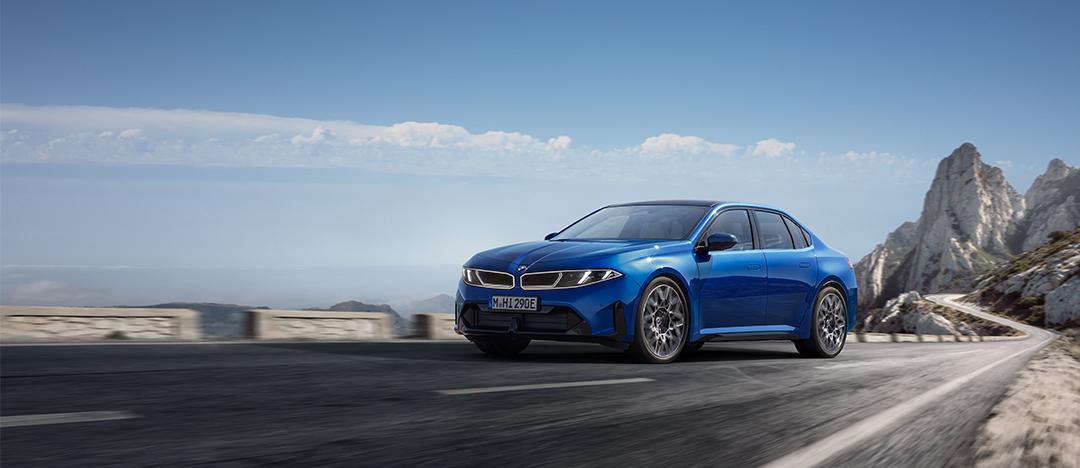 Blauer BMW i3 fährt auf einer kurvigen Bergstraße vor einer felsigen Berglandschaft.