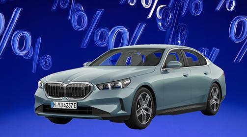 Eine dunkelgrau-grüner BMW 5er Limousine steht von vorne rechts vor einem leuchtend blauen Hintergrund, der mit schwebenden, glänzenden Prozentzeichen gefüllt ist, was auf ein besonderes Angebot oder einen Rabatt hinweist