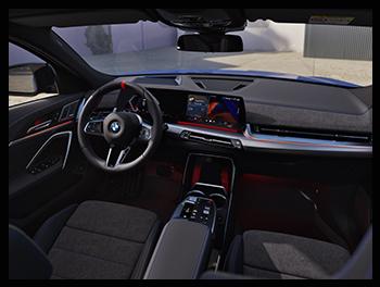 Das moderne Interieur mit dem Curved Display, einem M-Lederlenkrad mit roter 12-Uhr-Markierung, Sportsitzen und roten Akzenten in der Ambientebeleuchtung.