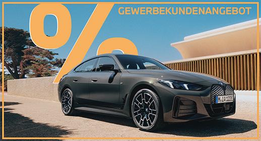 Das Bild zeigt eine Außenaufnahme eines dunklen BMW i4 Coupés im Sonnenschein, geparkt vor einem modernen Gebäude. Im oberen Teil des Bildes dominiert eine große, orangefarbene Werbegrafik mit ein Prozentzeichen und dem Text GEWERBEKUNDENANGEBOT.