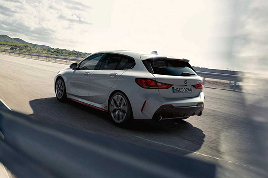 Weißer BMW 1er fährt dynamisch auf einer bergigen Landstraße, Rückansicht