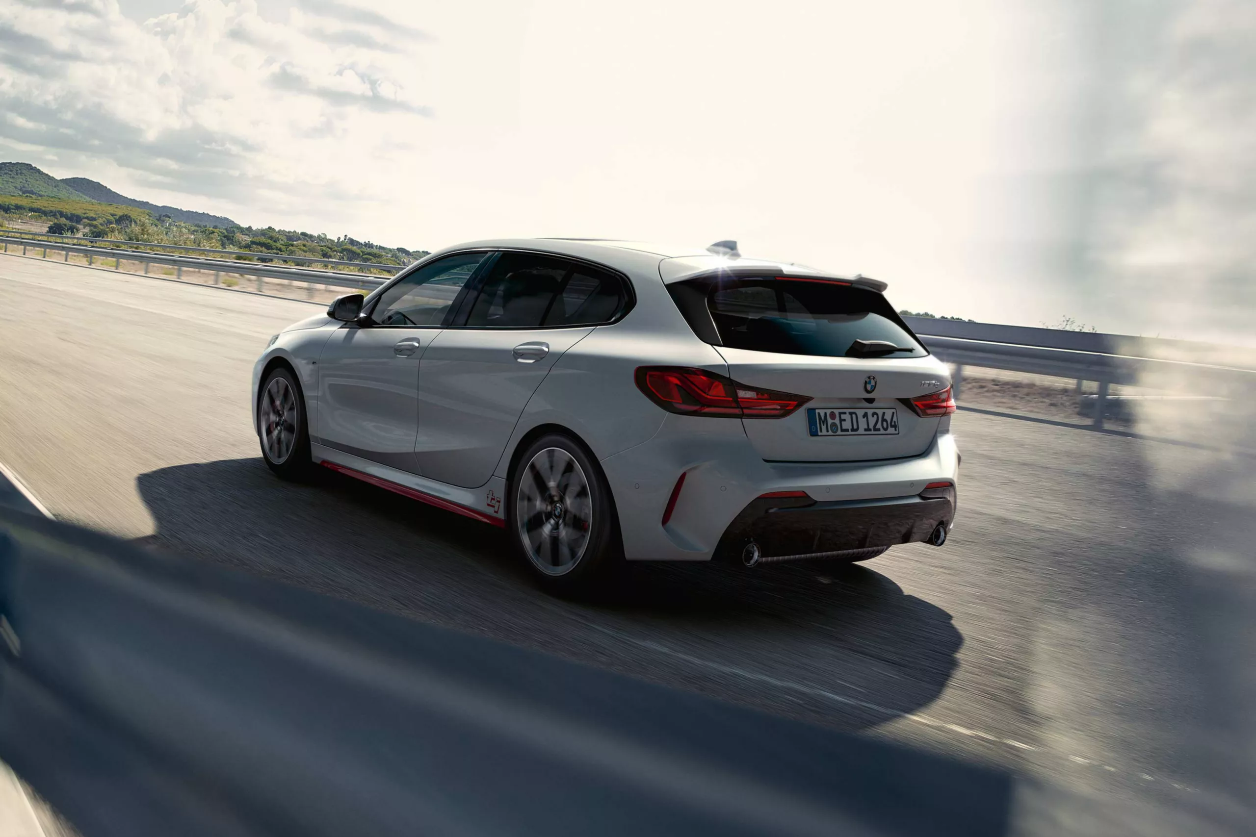 Leistungen BMW Müller Weißer BMW 1er fährt dynamisch auf einer bergigen Landstraße, Rückansicht